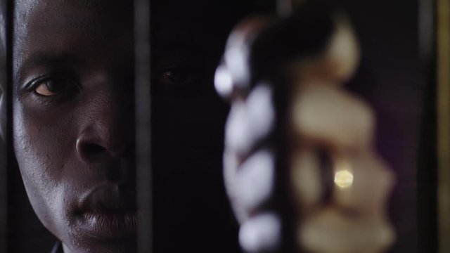 Young african prisoner behind bars staring at camera. Criminal,prison,law