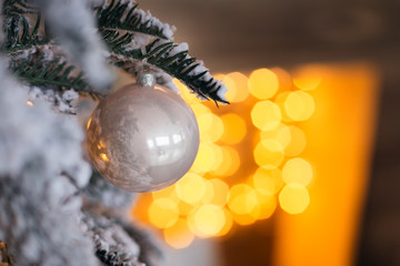 Close-up of a glass white ball on a branch of a Christmas tree against a background of blurred lights from the garland
