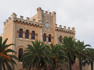 Fototapeta na wymiar view of the historic town hall in ciutadella menorca surrounded by palm trees and blue sunlit summer sky