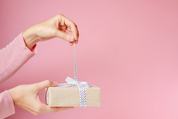 woman hands untie bow on gift box on a pink background
