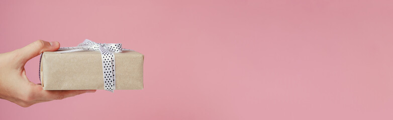 Woman hand holds gift box on a pink background, long banner with copy space