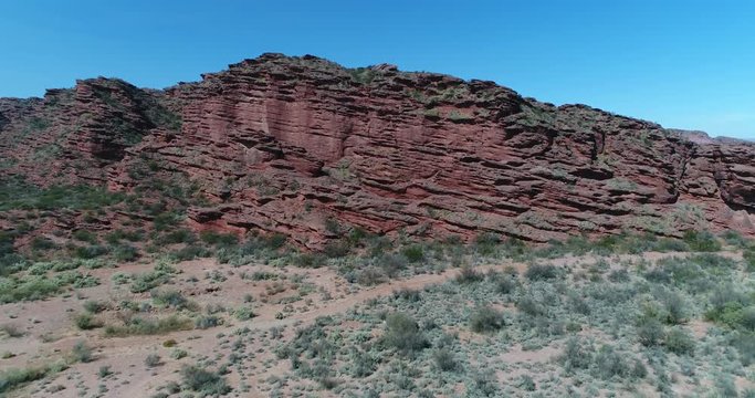 Aerial drone sene of red sandstone cliffs. Flying above ravines and canyons with native vegetation on the top. Dry rocky landscape at Rioja province, Argentina.
