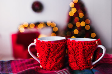 two cups with a knitted cover on the background of a room with a Christmas theme
