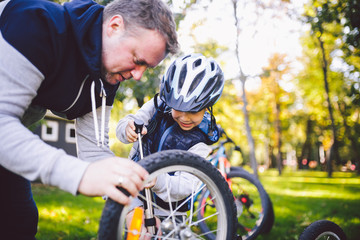 Father's day Caucasian dad and 5 year old son in the backyard near the house on the green grass on the lawn repairing a bicycle, pumping a bicycle wheel. Dad teaches how to repair a child's bike