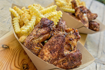 Portion of grilled chicken wings and chips in trays
