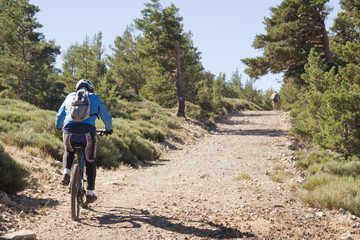 Women and mountain biking man riding on bikes in the mountains forest landscape. MTB track cycling couple enduro flow trail. Outdoor sports activity. Hard and steep climb