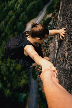 Frau klettert gef&auml;hrlich an Felsen. Eine Person reicht die Hand zur Hilfe.