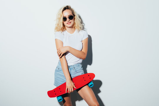 Hipster girl in holding a skateboard and looking at the camera isolated on white background