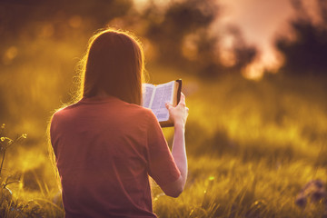 Girl reading the Bible at sunset