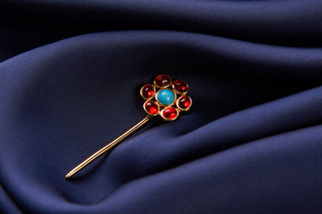 Gold hairpin with ruby precious stone on blue silk background with copy spce. Beautiful precious women's jewelry, close-up