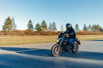Driver riding motorcycle on empty road in beautiful autumn forest.