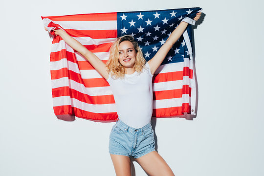 I love America. Happy young woman holding American flag and looking at camera while standing against white background