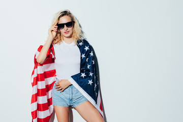 Young and carefree. Beautiful young blonde woman carrying American flag and smiling while celebrate...