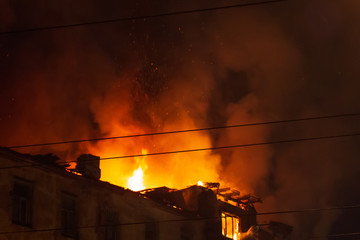 Burning building at night, roof of house in fire flames