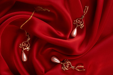 Beautiful precious women's jewelry, close-up. Pearl Golden Necklace and Earrings on red silk background with copy space