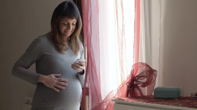Relaxed pregnant woman typing on smartphone and touching her belly