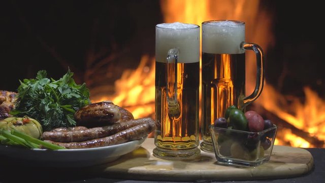 Two Beers, vegetables and grilled sausages on fire background, dolly shot