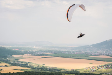 A white-orange paraglider flies over the mountainous terrain