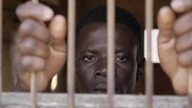 African young man behind bars staring at camera. Illegal migration,human rights
