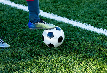 Fototapeta na wymiar classical black and white football ball on the green grass of the field and leg in sports shoes on it. Soccer game, training, hobby concept. with copy space 