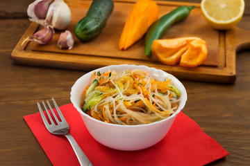 Rice noodles with sliced fresh vegetables in a white bowl, a metal fork on a red paper napkin.