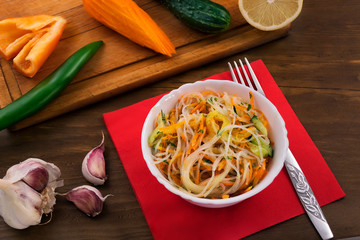 Rice noodles in a salad with sliced fresh vegetables, white bowl on a red paper napkin.
