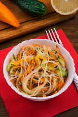 Rice noodles in white bowl, red napkin on wooden background.