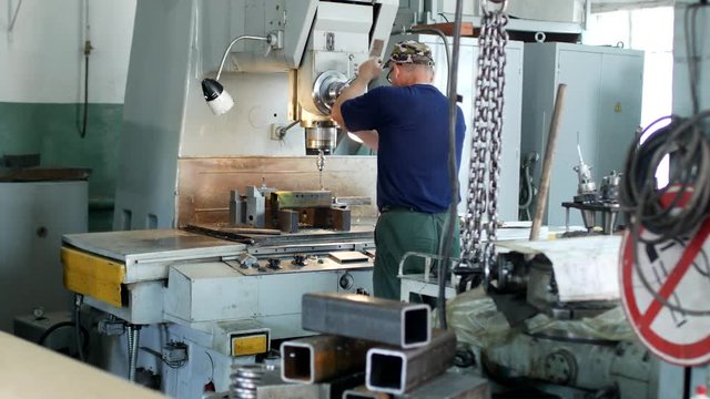 A man specializes a driller drilling holes on a drilling machine in a metal workpiece, a small business, private workshop, bench