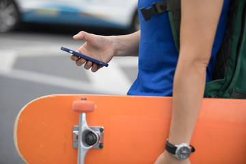 Woman with skateboard in hand using smartphone in modern city