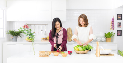 Beautiful Asian girl in casual dress is order fake fruit into wooden basket smile happily in a modern white kitchen.