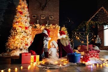 Happy family with a baby in a Santa Claus hat in a Christmas room in Christmas day.