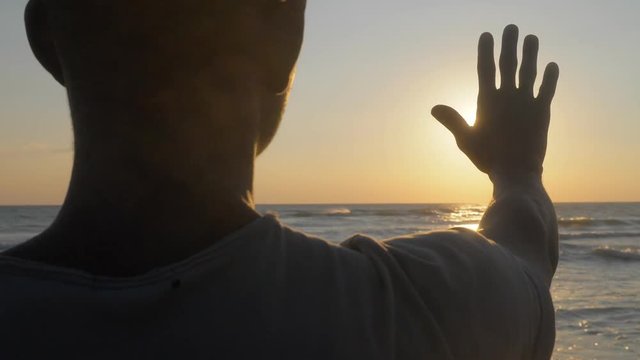young African black man on beach covering with his hand the sunlight at sunset