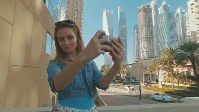 caucasian woman is taking selfies by mobile phone, outdoors in Dubai Marina in sunny day