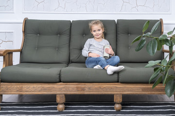 Cute little girl with a paper cup sitting on the sofa