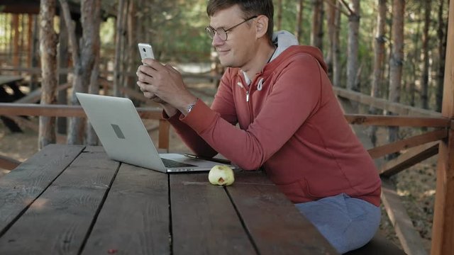 Mature man is working on his laptop outdoors in nature during his vocation aged forester using his laptop for e-mail checking while sitting at huge wooden table