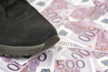 Male shoe stands on the background of money with a face value of 500 euro