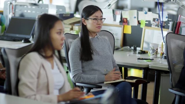 Medium shot of two young Asian women sitting in office and talking notes when listening to boss or colleague