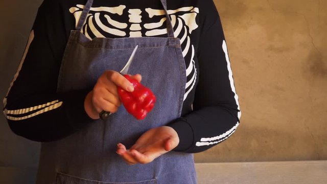 Young female cook in skeleton costume and apron cut red sweet peppers and clean to freeze. Hands close up.