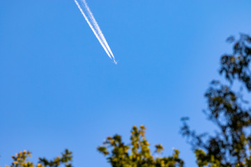 plane in the cloudless blue sky with a white contrail behind