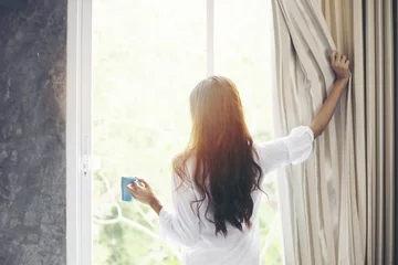 Poster Asian women drinking coffee and wake up in her bed fully rested and open the curtains in the morning to get fresh air on sunshine © tuiphotoengineer