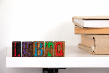 LGBTQ - word from colored wooden letters un the whitte shelf near books