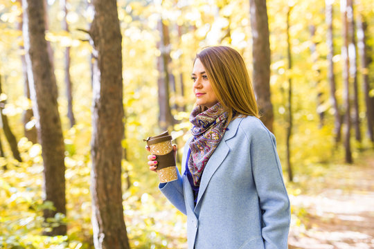 Attractive woman holding a cup of takeaway coffee cup on autumn street
