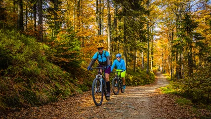 Schilderijen op glas Cycling, mountain biker couple on cycle trail in autumn forest. Mountain biking in autumn landscape forest. Man and woman cycling MTB flow uphill trail. © Gorilla