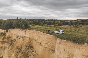 couple standing on cliff in overcast weather near white suv