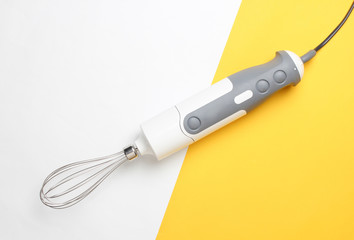 Electric hand blender whisk on white yellow pastel background. Top view, minimalism.