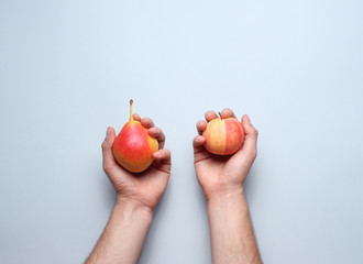 Hands holding ripe autumn pears and apple on a gray background. Top view. Minimalism.