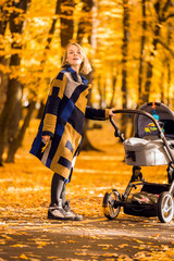 A young mother with a stroller walks through the autumn park. Walking with an infant in the open air in a pine forest. Newborn, family, child, parenthood.