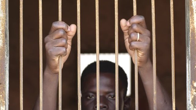 Jail, human rights,migration. Young african man behind prison's bars