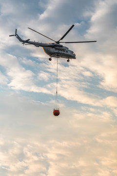 A fire fighter helicopter with a full basket of water flies against a beautiful sky. Rescue operation. Forest Fire Prevention