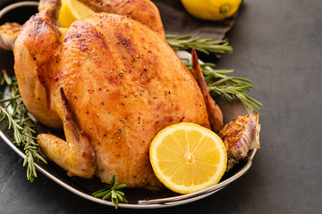 Roasted chicken with rosemary served on a metal plate with lemon on black table. Christmas turkey. Copy space.